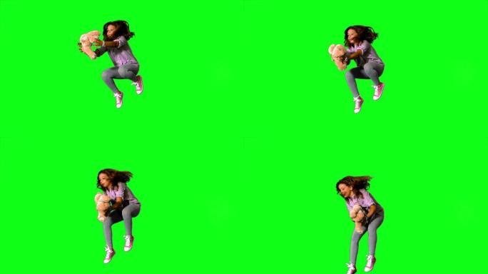 快乐的小女孩跳起来，在慢动作的绿色屏幕上抓住泰迪熊