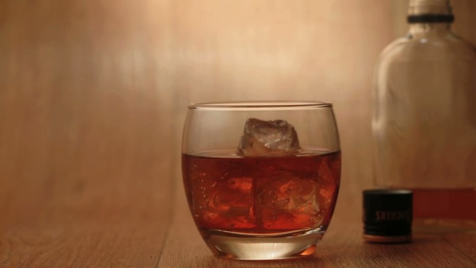 雪茄被抽在一个木制的表面上的岩石上的威士忌，瓶子的背景