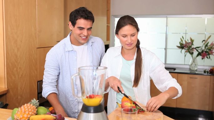 一个女人在丈夫的注视下往搅拌机里加水果