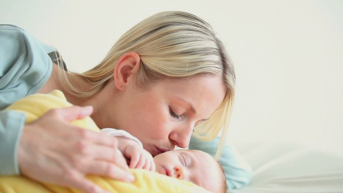 一名妇女抱着一个裹着黄色毯子的婴儿，然后亲吻他的脸颊