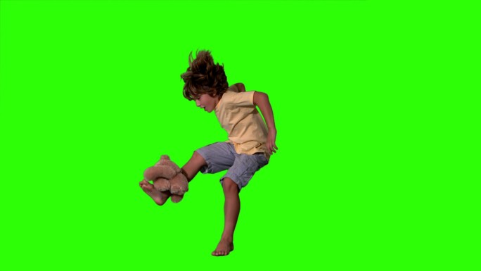 在慢动作的绿色屏幕上，小男孩跳起来踢泰迪熊