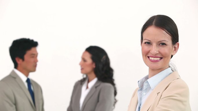 当同事们在白色背景下交谈时，女商人微笑着摆姿势