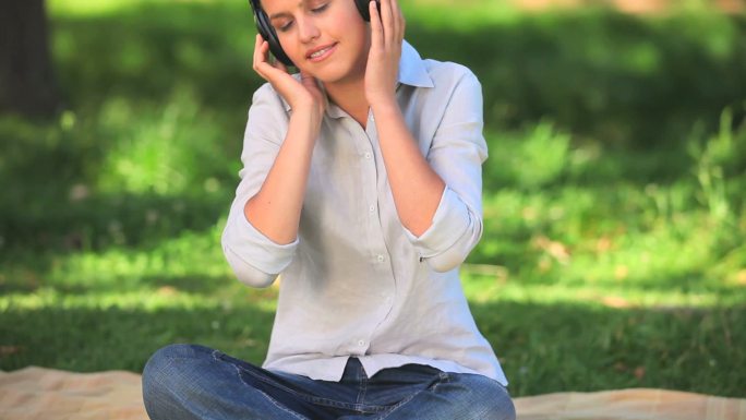 黑发女子戴着耳机在公园里听音乐