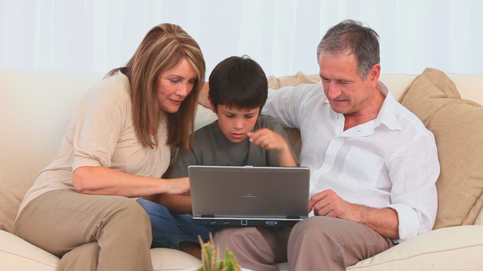 可爱的孩子和他的祖父母在沙发上使用笔记本电脑