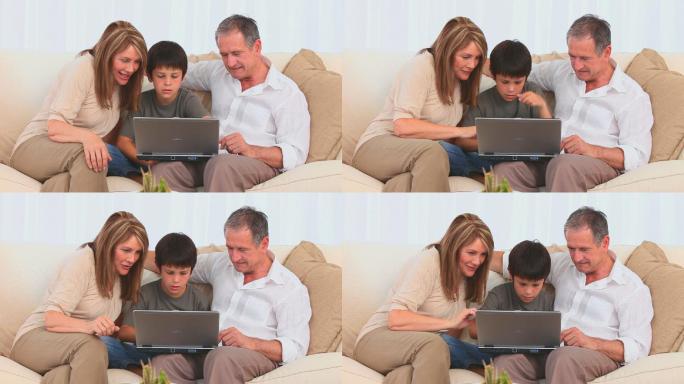 可爱的孩子和他的祖父母在沙发上使用笔记本电脑