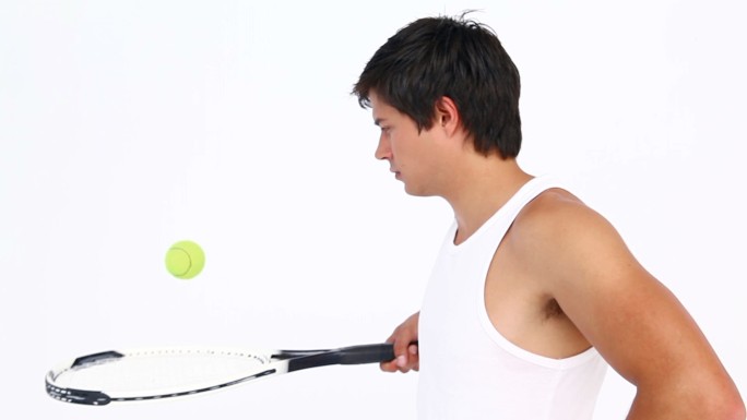 一个白人男性用网球拍颠球在白色背景下