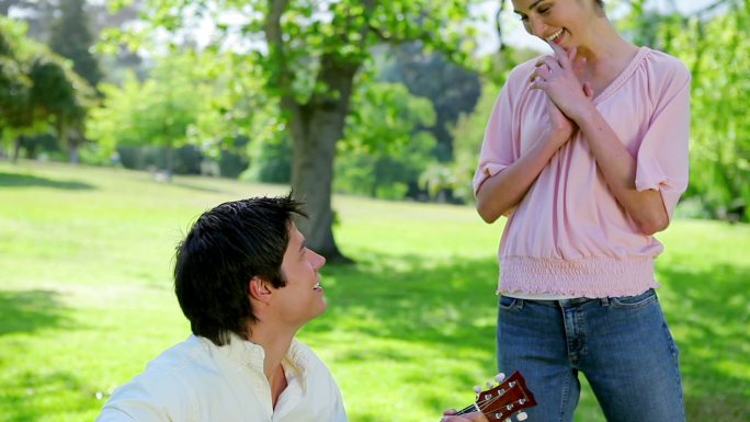 微笑的男人用他的吉他在公园里为他的女朋友演奏音乐
