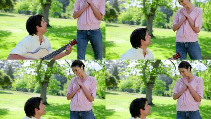 微笑的男人用他的吉他在公园里为他的女朋友演奏音乐