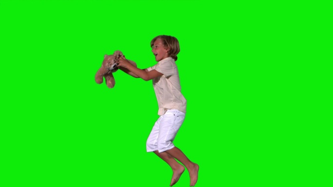 可爱的男孩跳跃和捕捉泰迪熊在绿色背景的慢动作