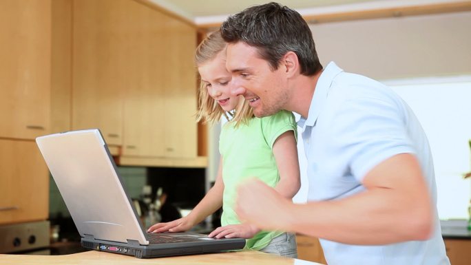 女儿在用笔记本电脑，而父亲在看厨房