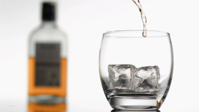 威士忌以超慢的动作倒入玻璃杯中，背景是一个瓶子和冰块