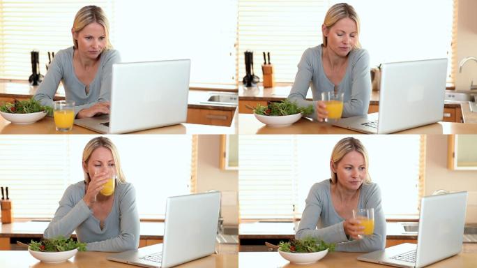 一个女人边喝橙汁边看笔记本电脑