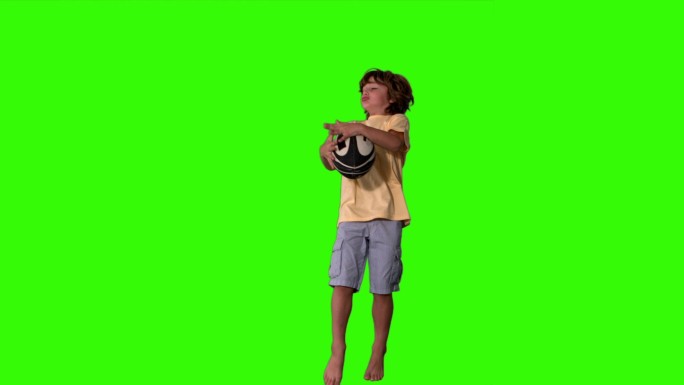 在绿色屏幕上，小男孩跳起来接住橄榄球的慢动作