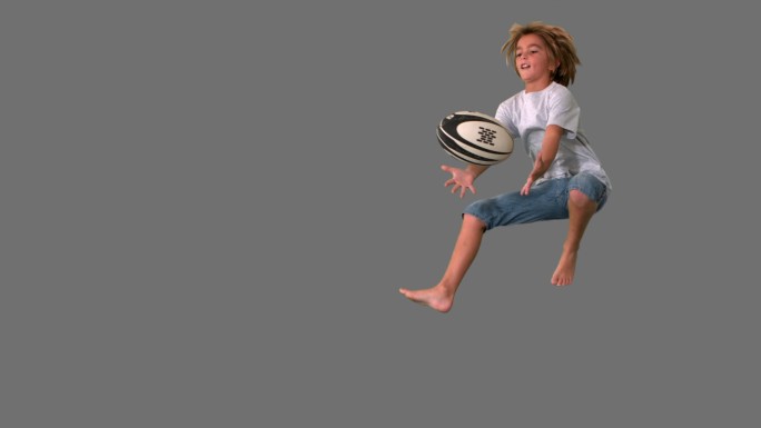 在灰色屏幕上，男孩跳起来接住橄榄球的慢动作