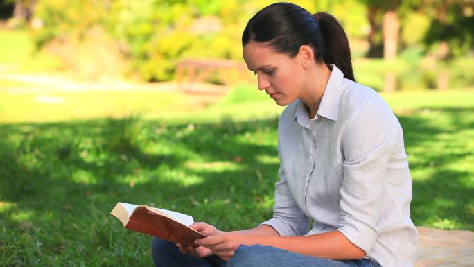 一个女人坐在公园的草地上看书