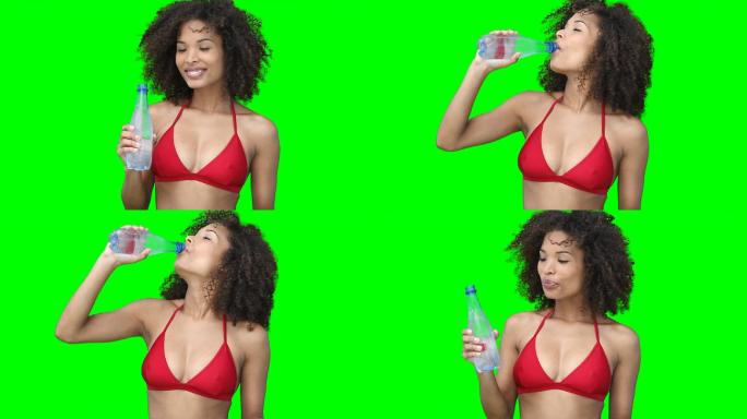 一个女人微笑着喝着瓶子里的水，背景是绿色