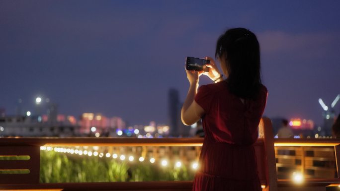 夏天夜晚江边栏杆处在拍照的女孩