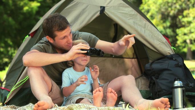 在公园里，父子俩用双筒望远镜看帐篷外的东西