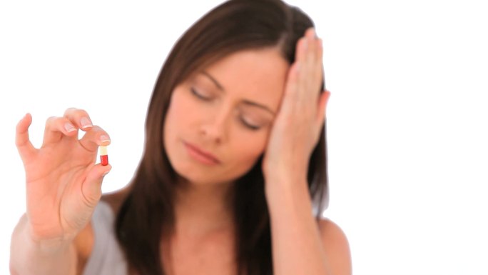 一个头痛的女人，手里拿着一片药丸，孤立地放在白色的背景上