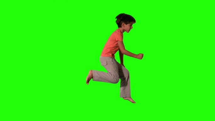男孩跳跃在绿色屏幕的侧视图在慢动作