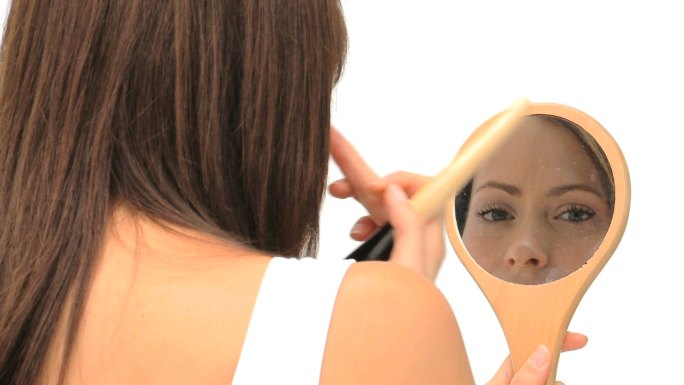 漂亮的黑发女人正在用镜子和刷子化妆