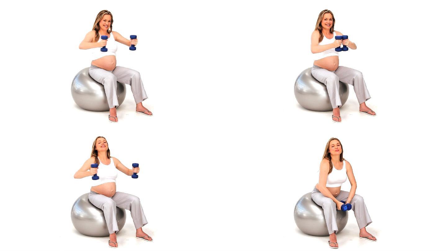 一个在健身球上拿着哑铃做运动的孕妇，在白色背景下
