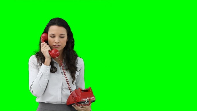 一位在绿色背景下使用红色电话的女商人