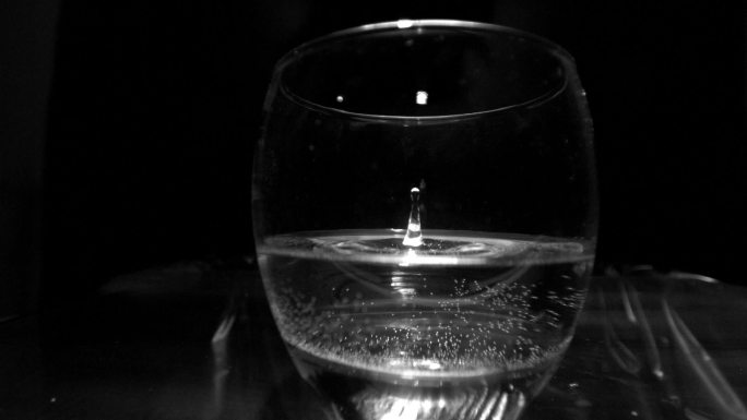 在黑色背景的慢镜头中，一滴水滴入玻璃杯