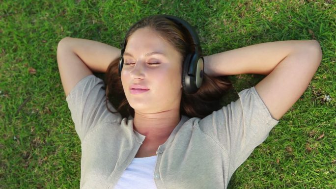 公园里一个戴着耳机躺在草地上的女人