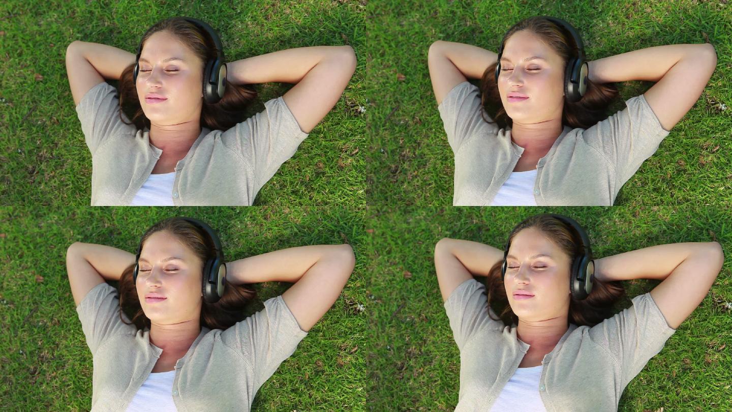 公园里一个戴着耳机躺在草地上的女人