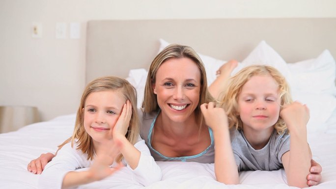 母亲和她的两个孩子躺在床上对着镜头挥手