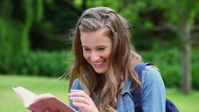 微笑的年轻女子在一个公园里看书