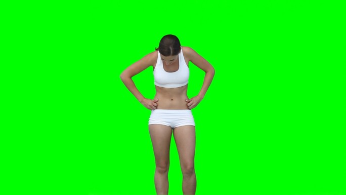 一个穿着训练服的女人在绿色背景前检查自己的身材