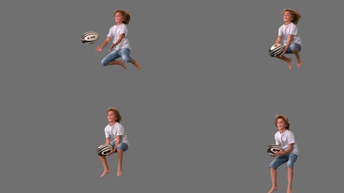 在灰色背景的慢镜头中，男孩跳跃着去接橄榄球