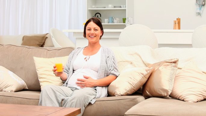 一个孕妇坐在沙发上喝着橙汁