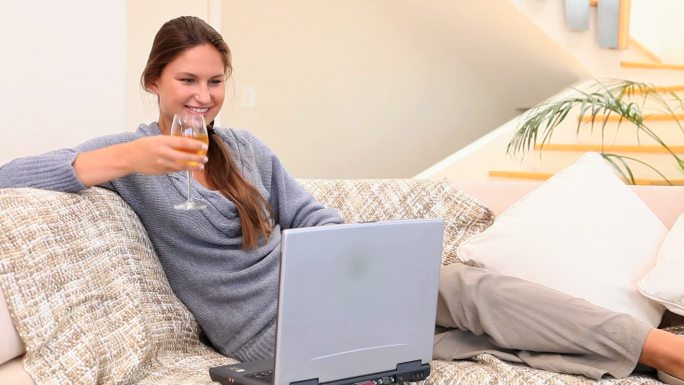 一个女人坐在沙发上一边喝着酒一边用笔记本电脑聊天