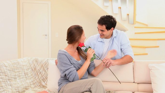 一名男子在客厅向未婚妻献上一朵红玫瑰