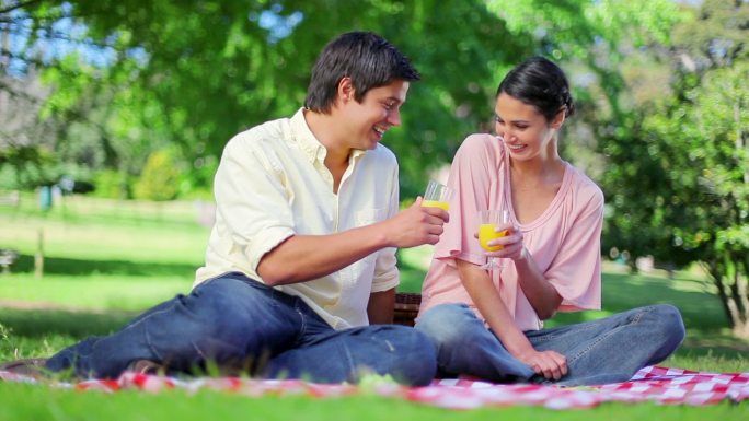 一对笑嘻嘻的情侣在公园里喝橙汁