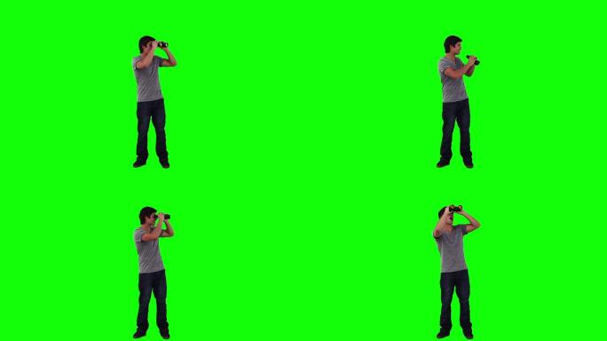 一个男人在绿色的背景下用双筒望远镜向四周看