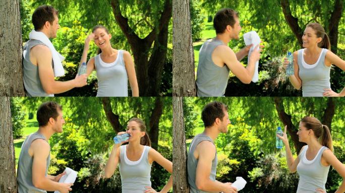 运动情侣慢跑后在树下分享一瓶水和一条毛巾
