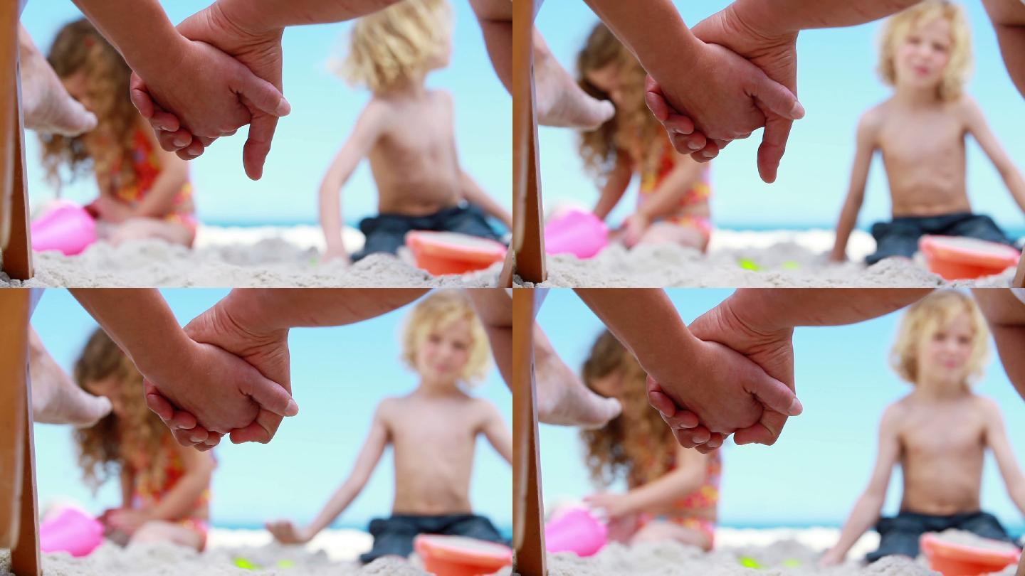 牵手的父母看孩子们在海滩上堆沙堡