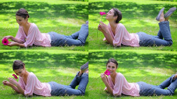 微笑的女人躺在草地上，手里拿着一朵花在乡下
