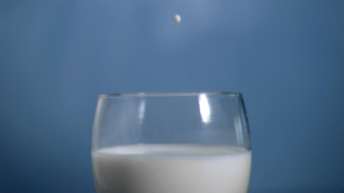在蓝色背景下，牛奶中液滴以超慢的运动下落