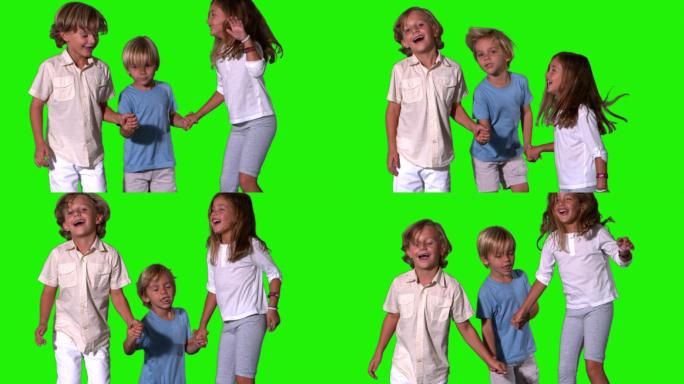 兄弟姐妹手牵着手，在绿色屏幕上慢动作跳跃