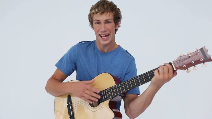 微笑的男人拿着他的原声吉他在一个白色的背景