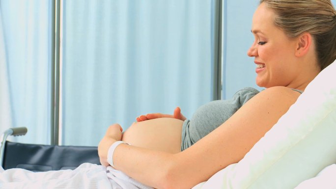一名孕妇在诊所的床上抚摸着自己的肚子