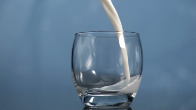 牛奶在蓝色背景下以超慢的动作流入玻璃杯