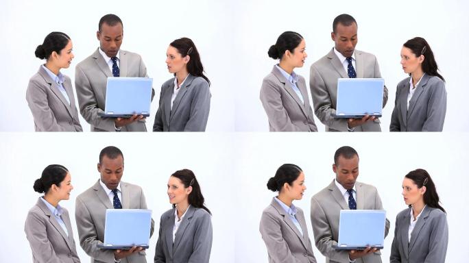 一名手持笔记本电脑的男子与同事在白色背景下交谈