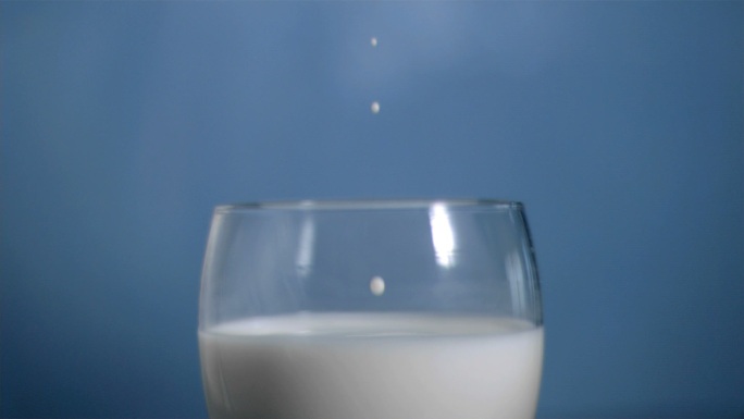 牛奶滴入玻璃杯慢镜头，在蓝色背景下