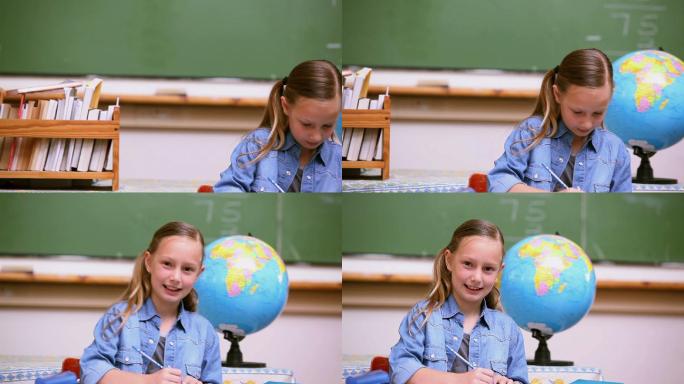 微笑的小学生在她的笔记本上写在教室里